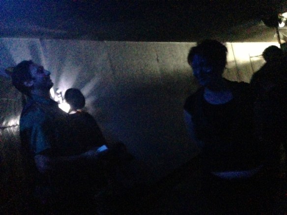 A tall poet in the dark tunnel with shadowy figures and light behind him, a grainy strange atmospheric image