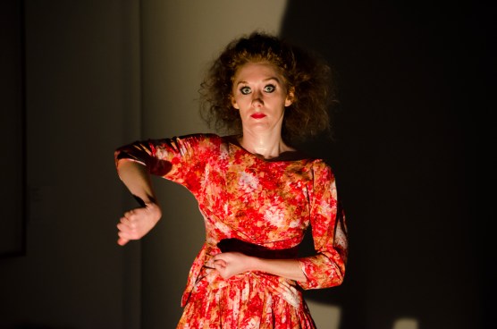 A woman in in a bright orange dress, it seems she is making something with repetitive movements over and over