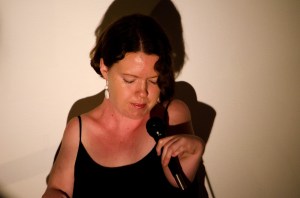 A woman in shadow with her head bowed down and eyes closed, singing