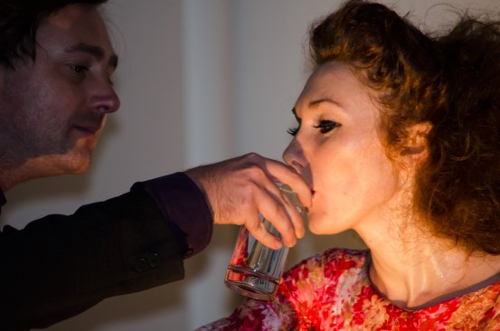 A man holds a glass of water for her to drink water, and she drinks