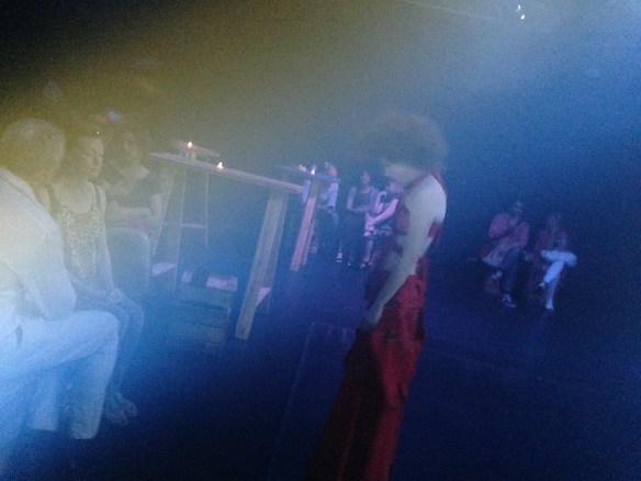 Smoky dark coloured lights room with female performer very close to audience